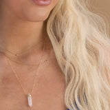 Close-up of a woman's neck wearing a Diamond Layering Necklace, a 14k Gold Asymmetrical Letter Necklace - C and The Love Retreat Necklace, all in yellow gold, with her blonde hair.