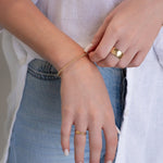 A close-up of a woman's arm and hands wearing a Little Bubble Bracelet, two Delicate Beaded Bands, a Twinkle Twinkle Ring and a Thick Band, with a white shirt and blue jeans. 