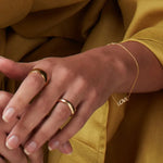 A close-up of a woman's hand and arm wearing a Love Bracelet, a Thick Band and a Tube Ring, in mustard clothing. 