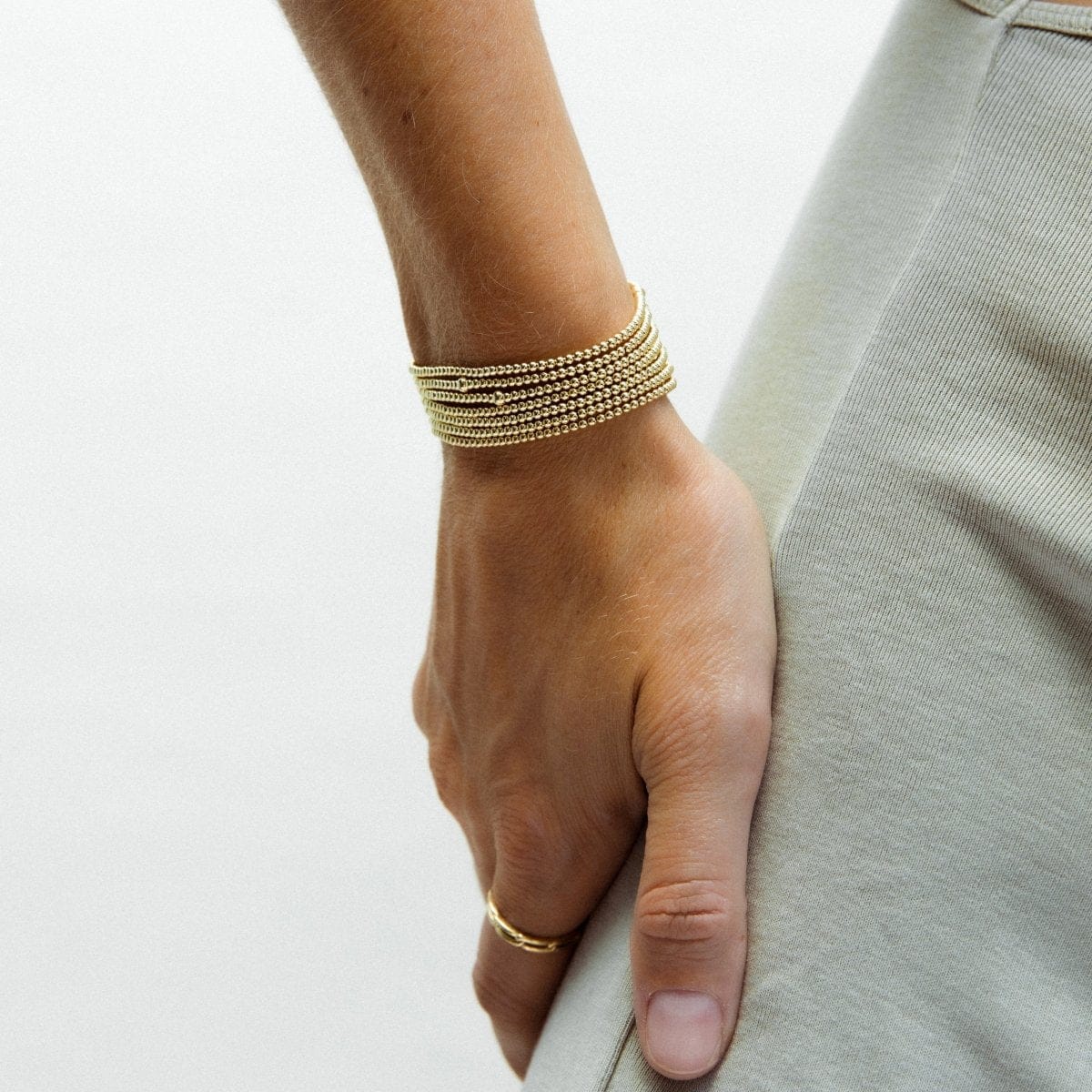 A hand wearing multiple stacked Mini Bubble Bracelets and a Link Ring, resting on the person’s torso in a light sage green top.