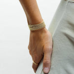 A hand wearing multiple stacked Mini Bubble Bracelets and a Link Ring, resting on the person’s torso in a light sage green top.