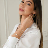 A woman wearing The Lily Bouquet Bracelet, Baroque White Pearl Bangle, Little Bubble Bracelet, Perla Pinky Ring, Pearl Drift Threader and The Lily Bouquet Necklace, styled with a white shirt. 