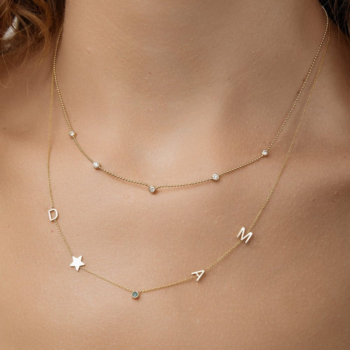 Close-up of a neck wearing a Quintet Diamond Layering Necklace and a Custom Gold Necklace - 5 Letters in yellow gold. 