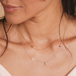 A close-up of a woman’s neck wearing a 14k Gold Asymmetrical Charm Necklace - Star of David with a bead chain, and a Custom Gold Necklace - 5 Letters (L, S, a hand, K and a birthstone), both in yellow gold.