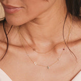 A close-up of a woman’s neck wearing a 14k Gold Asymmetrical Charm Necklace - Star of David with a bead chain, and a Custom Gold Necklace - 5 Letters (L, S, a hand, K and a birthstone), both in yellow gold.