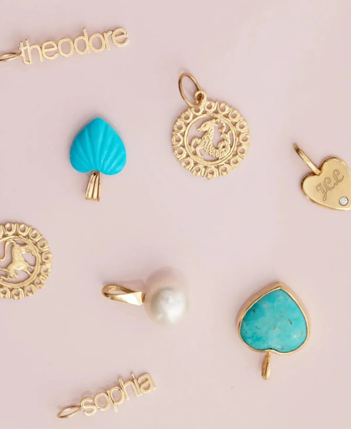 Several yellow gold and turquoise pendants and charms, including Zodiac Pendants, Petite Nameplate Pendants, a Perla Pendant, a Turquoise Heart Charm, an Etched Turquoise Heart Charm and an Engraved Heart Charm on a light pink background. 
