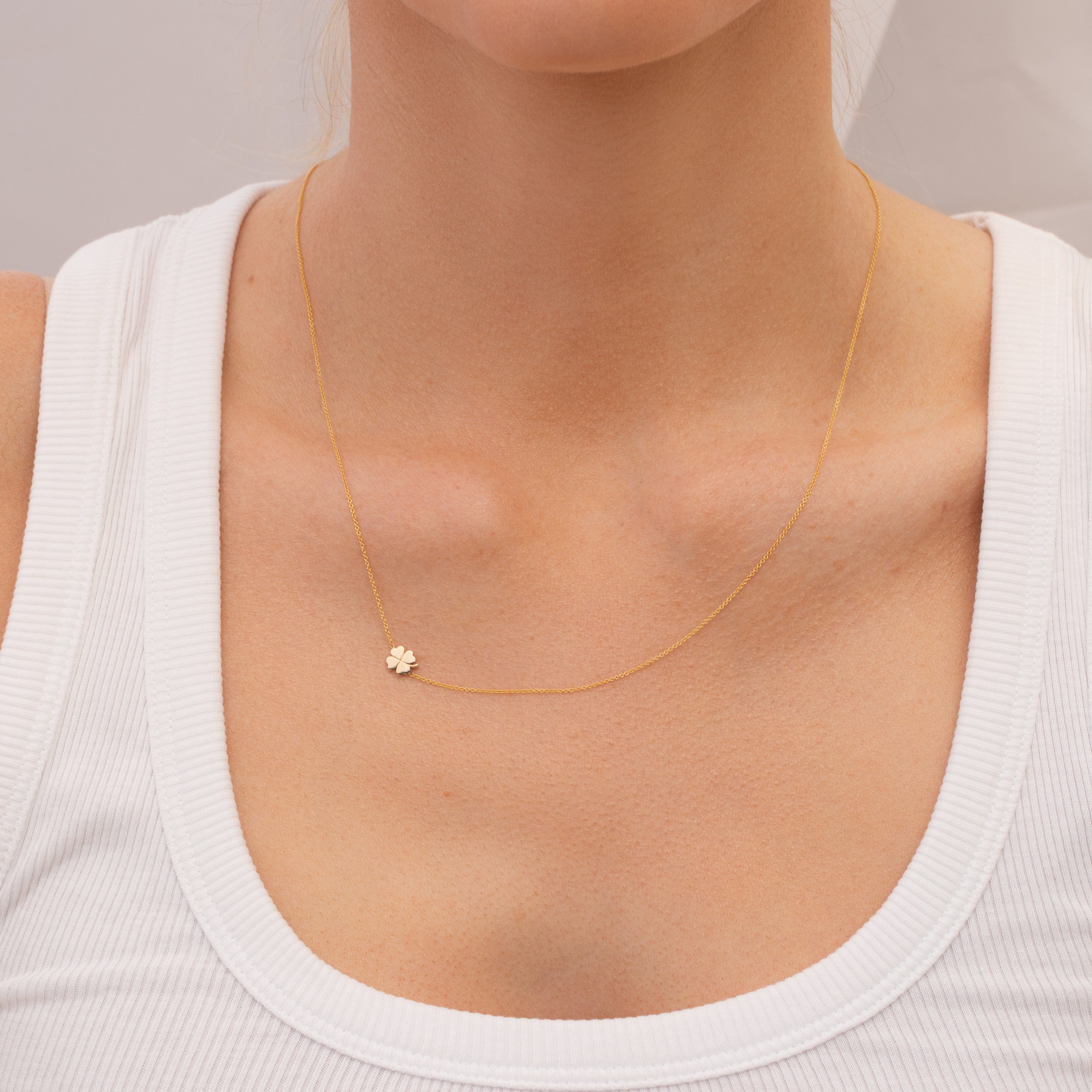 Gold necklace with a small gold four leaf clover charm worn by a person in a white top.