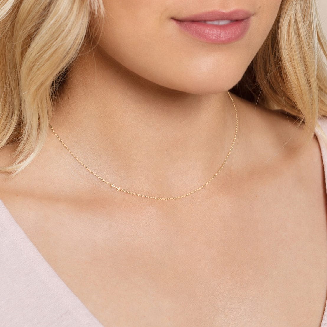 Close-up of a woman's neck wearing a white gold necklace with a letter I charm.