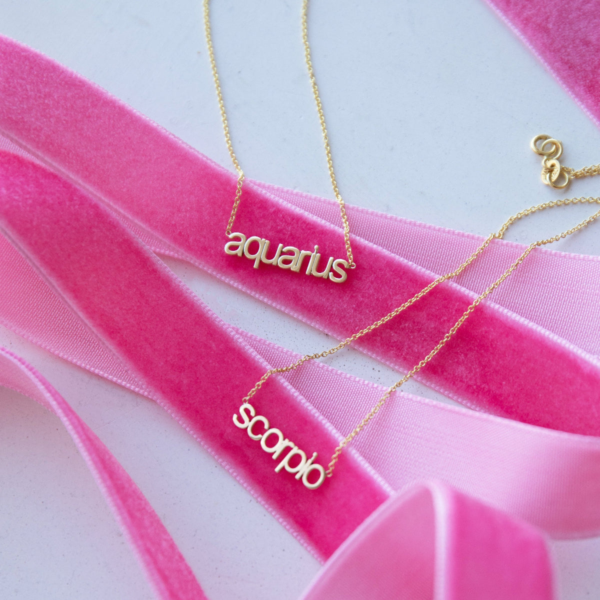 zodiac nameplate necklaces on pink velvet ribbon on a white background