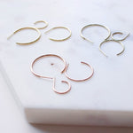 Crescent Hoops / Small, Medium and Large in rose, white and yellow gold on a white surface. 