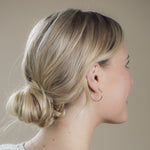 Side profile of a woman wearing a Crescent Hoop / Large with her blonde hair in a bun against a neutral background. 