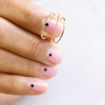 A hand holding a yellow gold Delicate Band, Delicate Beaded Band and Delicate Twist Band with pink nails against a white background. 