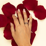 A hand wearing two The Rose Bouquet Rings with dark red petals in the background. 