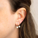 Close-up of Charmed I'm Sure Hoops in Heart and Star shown on a brunette woman's ear against a light grey background. 