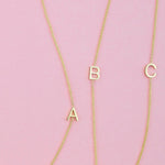 Three gold necklaces with single letter charms A, B and C on a pink background. 