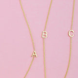 Three gold necklaces with single letter charms A, B and C on a pink background. 