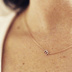 A close-up of a woman's neck wearing a gold necklace with a letter E charm. 