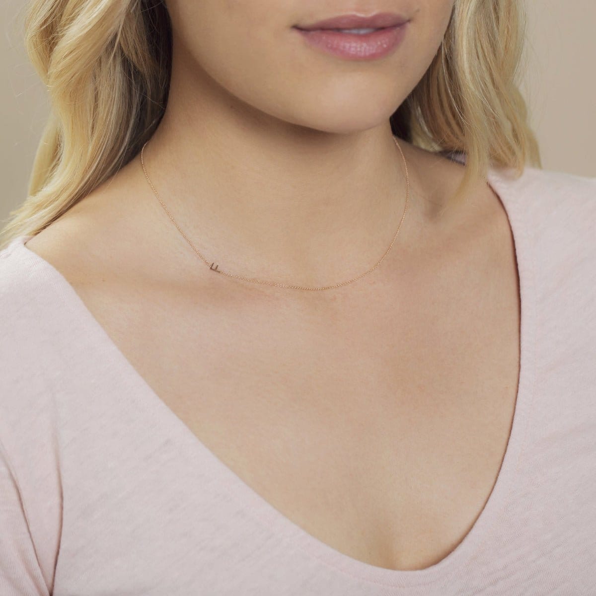 Close-up of a woman's neck wearing a gold necklace with a letter F charm. 