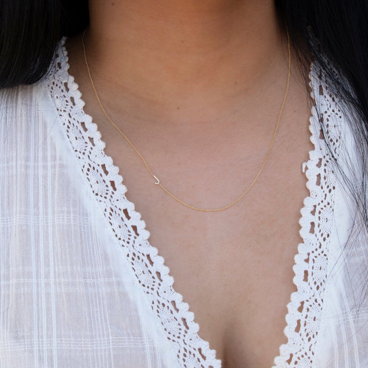 A close-up of a woman's neck wearing a gold necklace with a letter J charm. 