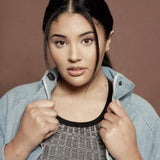 A woman wearing a dark grey top and denim jacket, a necklace with a letter W charm and stud earrings.