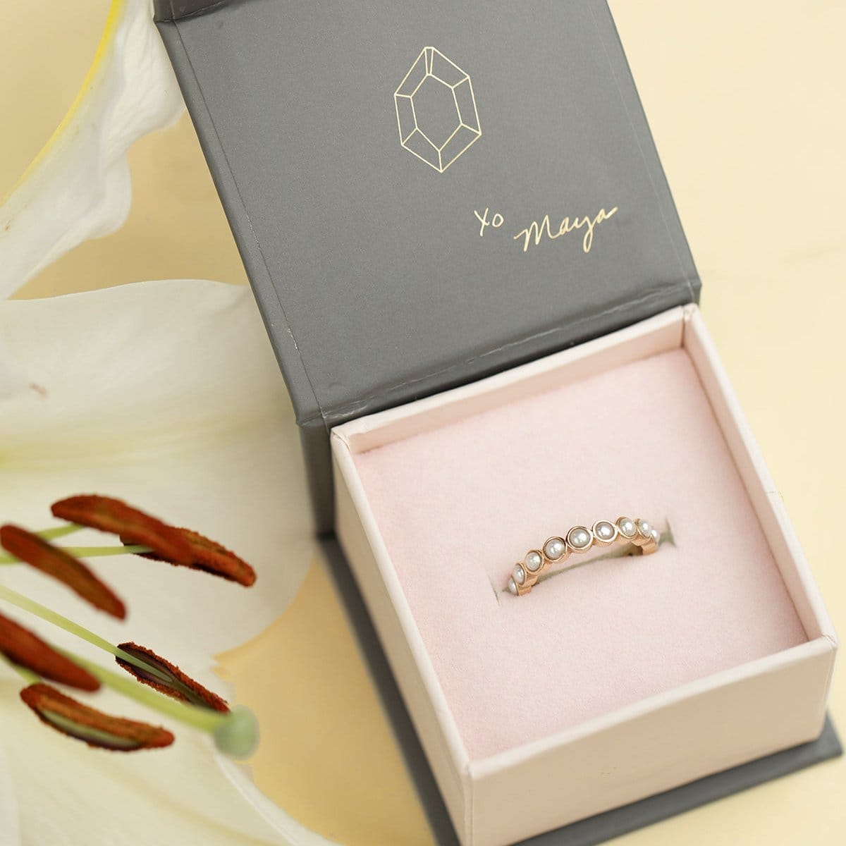 A Lily Bouquet Ring in a Maya Brenner jewelry box against a light yellow background with a painted lily. 