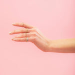 A hand wearing several Link Rings in yellow gold, rose gold and white gold against a light pink background. 