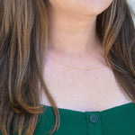 A close-up of a woman's neck wearing a gold necklace with a letter C charm. 