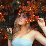 A woman wearing a necklace with a M letter charm surrounded by red flowers. 