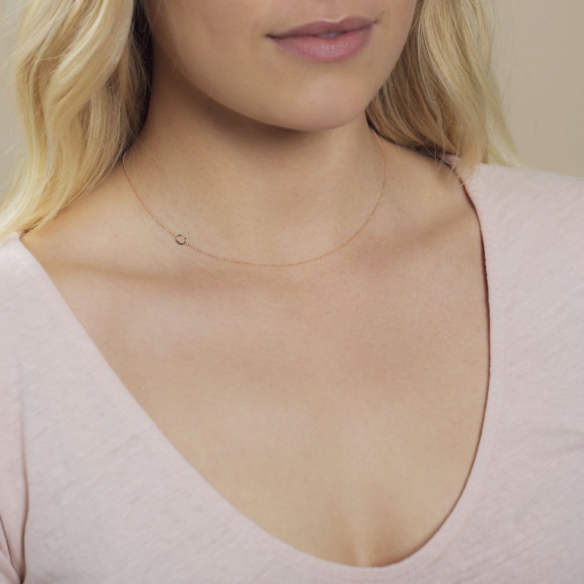 A close-up of a woman's neck wearing a gold necklace with a letter C charm. 