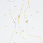 Three gold necklaces with single letter charms, being J, B and W, featuring multiple little gemstones on a white background.