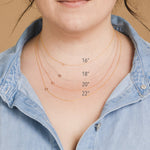 A close-up of a woman's neck wearing 4 necklaces with single letter charms A, B, C and D in various lengths. 
