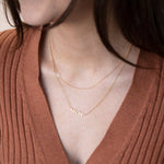 A close-up of a woman’s neck wearing two gold necklaces, one with a letter W charm and the other with the word MADRE.