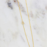 A gold necklace with a pave letter A charm  on a marble background. 