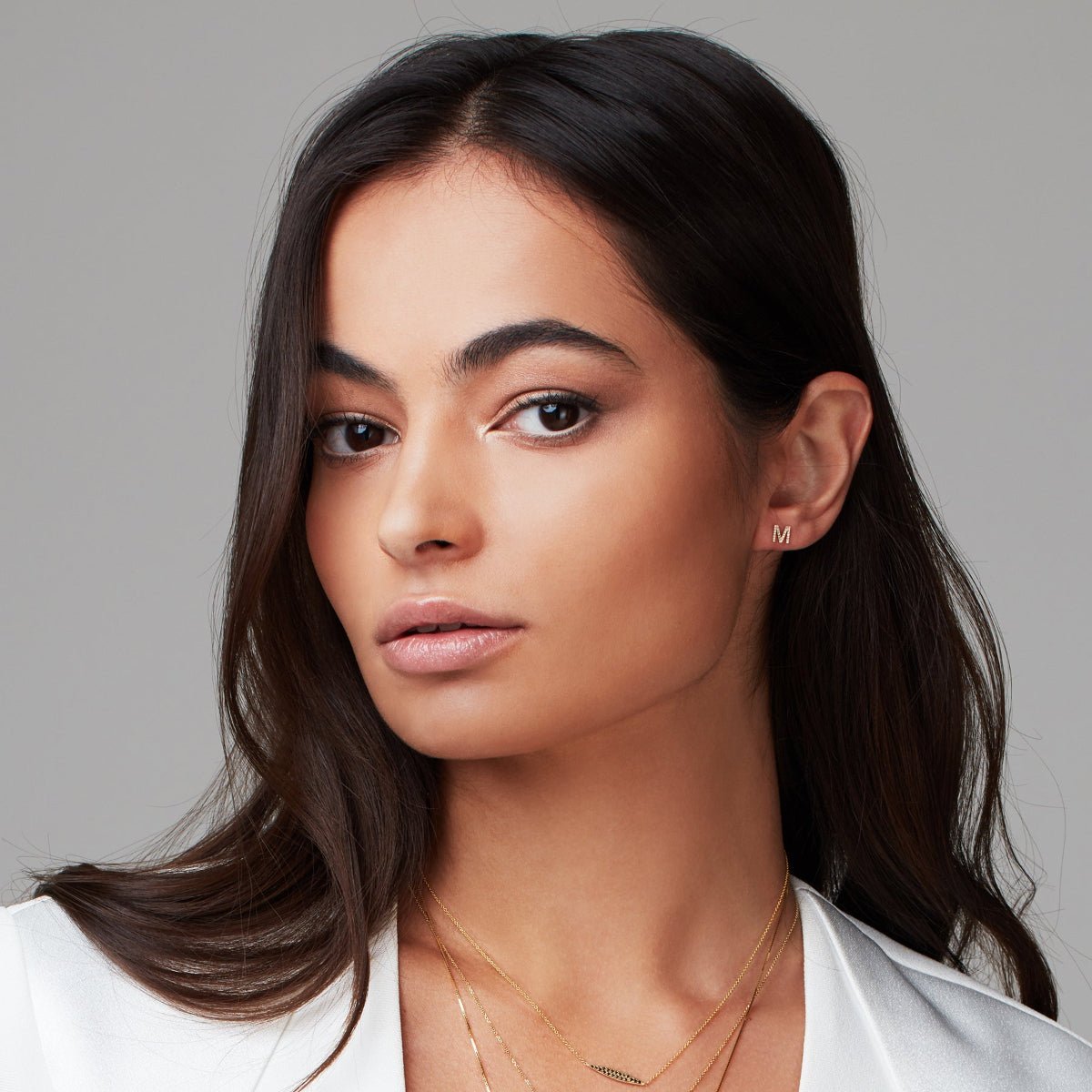 Woman wearing a gold pave single letter M stud. 