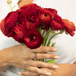 A woman's hand wearing two The Tulip Bouquet Rings with a white top, holding red flowers.