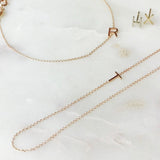 A necklace, bracelet and two stud earrings, each with its own letter charm – R, T, H, and X against an off white marble background. 