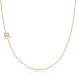 A rose gold necklace with a pave letter R charm on a white background. 