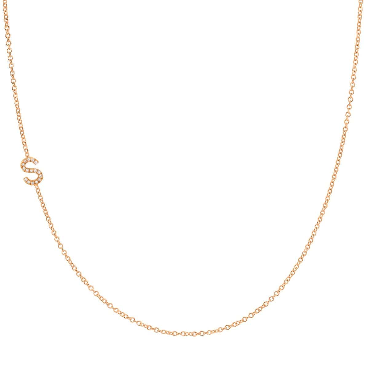 A rose gold necklace with a pave letter S charm on a white background. 
