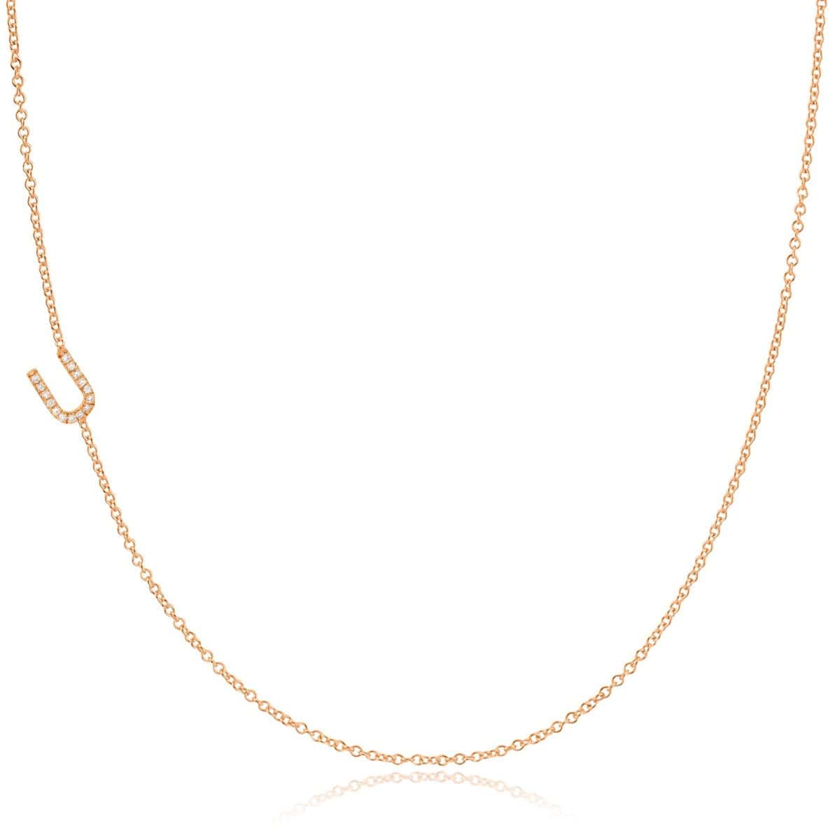 A rose gold necklace with a pave letter U charm on a white background. 