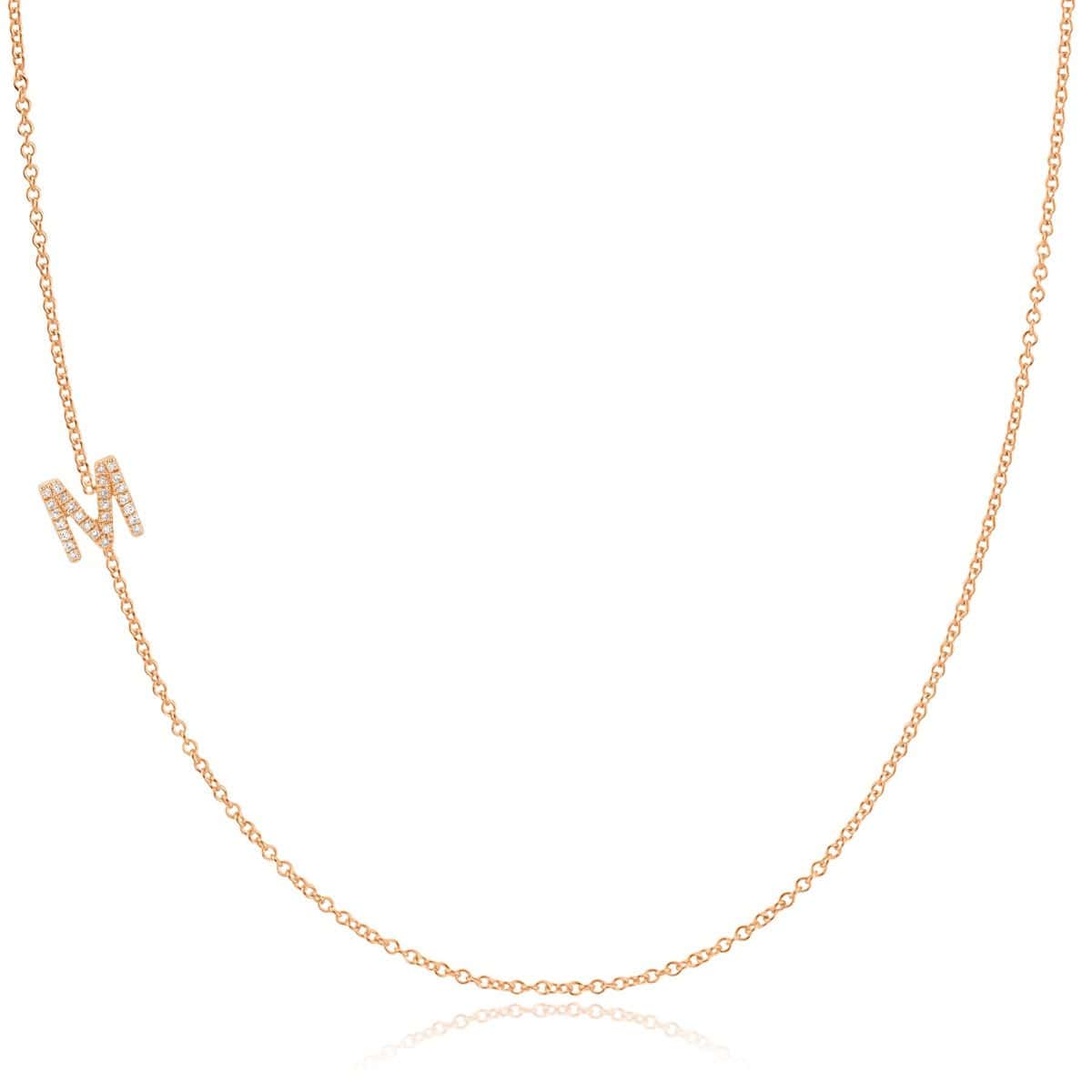A rose gold necklace with a pave letter M charm on a white background. 