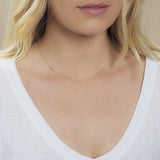 A close-up of a woman's neck wearing a 14k Gold Asymmetrical Number Necklace - 2 in rose gold, with blonde hair, styled with a white top. 