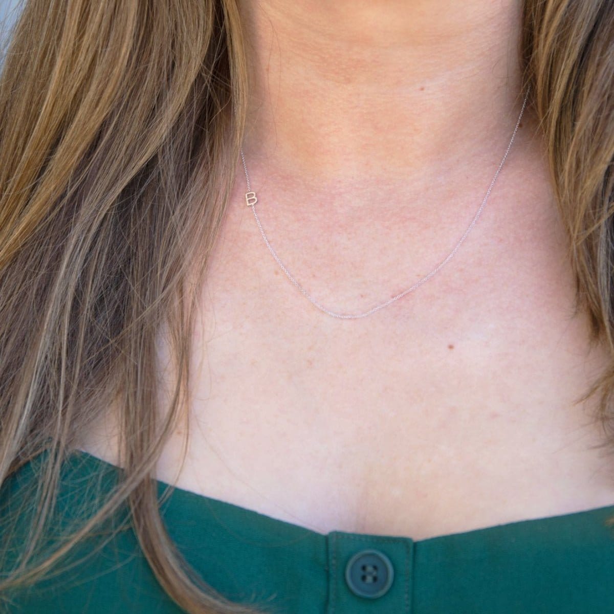 A close-up of a woman's neck wearing a white gold necklace with a B letter charm. 