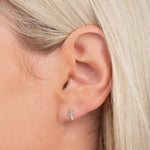 Close-up of a Charm Stud - Cross in white gold in a blonde woman’s ear.