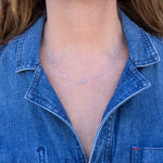 A close-up of a woman's neck wearing a Custom Gold Necklace in white gold with seven letter charms (M, A, B, M, H, B and T) and a blue denim shirt. 