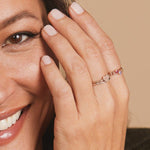 Close-up of a woman's hand wearing a white gold Heartfelt Ring and three Birthstone Rings, against light neutral background. 