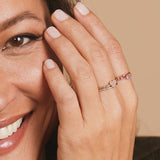 Close-up of a woman's hand wearing a white gold Heartfelt Ring and three Birthstone Rings, against light neutral background. 