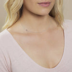 Close-up of a woman's neck wearing a white gold necklace with a letter H charm. 