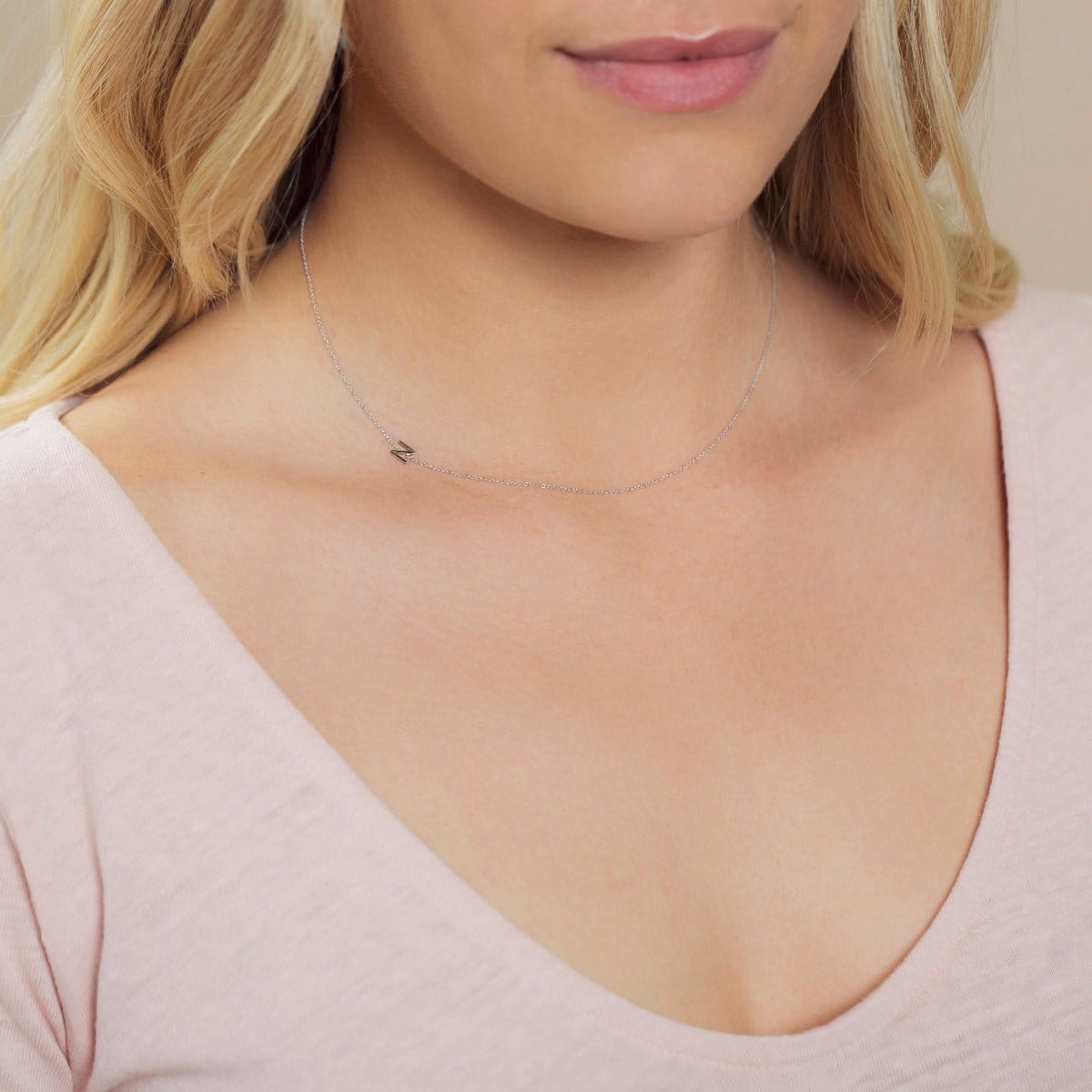 Close-up of a woman's neck wearing a white gold necklace with a letter N charm. 