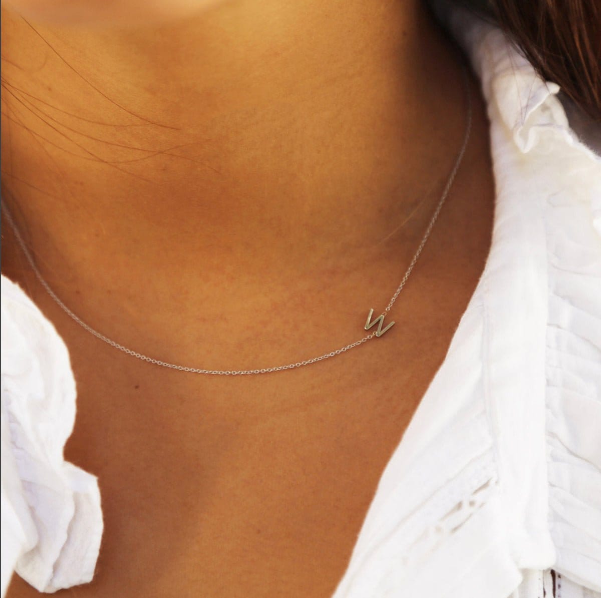 A close-up of a woman's neck wearing a white gold necklace with a letter W charm. 
