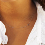 A close-up of a woman's neck wearing a white gold necklace with a letter W charm. 